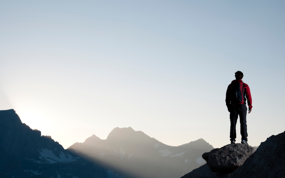 A person standing on top of a mountain with mountains in the background.