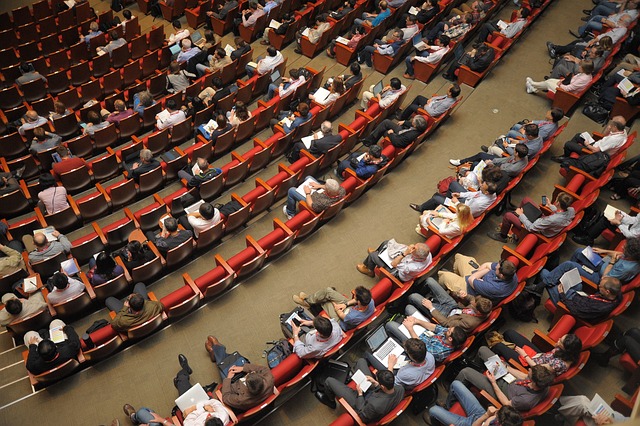 A large group of people sitting in rows on red seats.